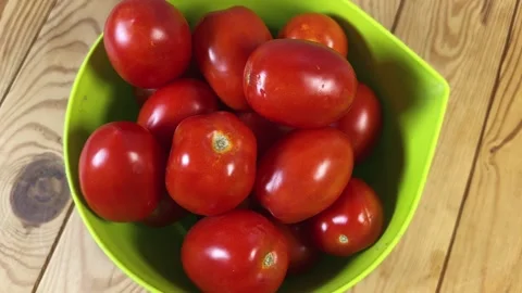 Red plum tomatoes in green plastic bowl on rustic table Stock Footage 346473602