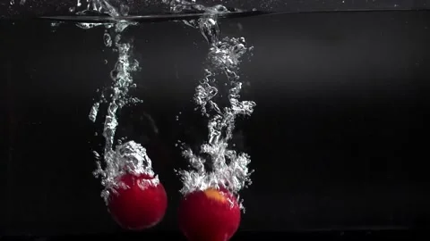Red plums fall into the water with splashes, slowly sinking to the bottom Stock Footage 133341157