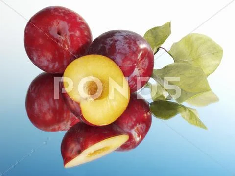 Red plums, whole and halved, with leaves Stock Photos