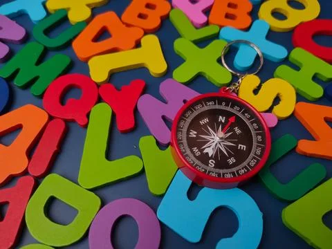 Red pocket compass keychain lying on a scattered arrangement of colorful wo.. Stock Photos