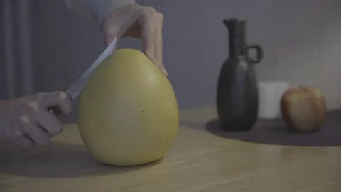 Red Pomelo Being Sliced with small knife on Table, Apple and Vase Silhouetted in Stock Footage 265099681