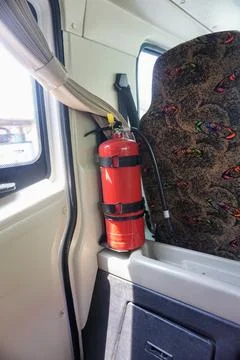 A red portable fire extinguisher is mounted inside the cabin of a passenger bus. Stock Photos