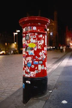 Red post box covered with stickers on city street at night in Edinburgh Stock Photos