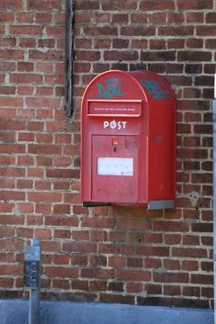 A red post box mounted to a brick wall next to a parking meter Stock Photos
