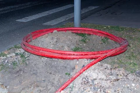 Red protective pipe for underground electrical cables on a city street Stock Photos
