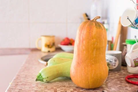 Red pumpkin is on the table on the background of green zucchini Stock Photos