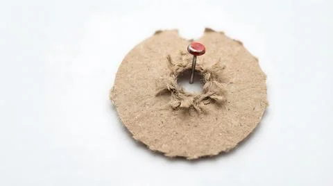 Red push pin stuck through a circular piece of textured brown cardboard on .. Stock Photos