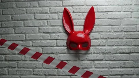 Red rabbit mask on a white brick texture wall and red and white signal tape Stock Footage 142734585