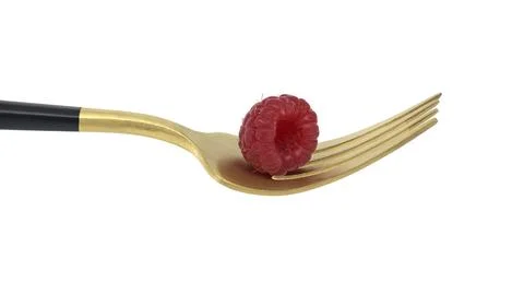 Red raspberry arranged on gold fork with a black handle, set against a white Photos