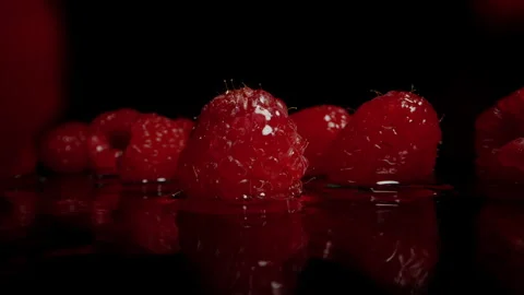 Red raspberry berries falling onto a wet black surface, splashing water around. Stock Footage 270425788
