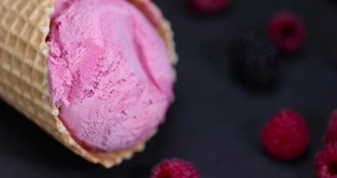 Red raspberry ice cream in a waffle cone on a black background, delicious sweet Stock Footage 295639885