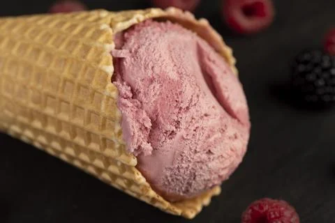 Red raspberry ice cream in a waffle cone on a black background Stock Photos
