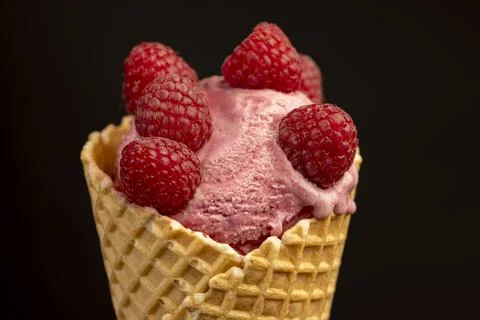 Red raspberry ice cream in a waffle cone on a black background Stock Photos