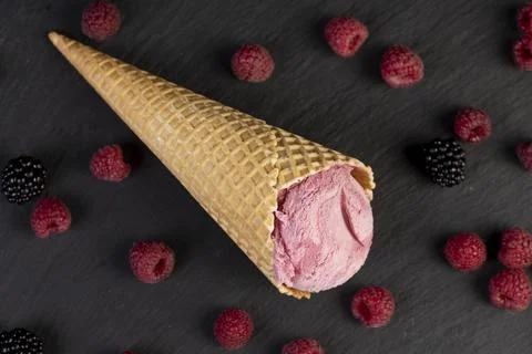 Red raspberry ice cream in a waffle cone on a black background Stock Photos