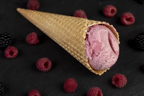 Red raspberry ice cream in a waffle cone on a black background Stock Photos