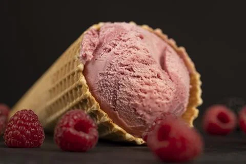 Red raspberry ice cream in a waffle cone on a black background Stock Photos