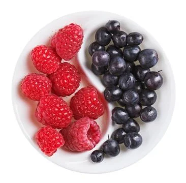 Red raspberry versus black bilberry in yang yin shaped plate, isolated on whi Foto stock