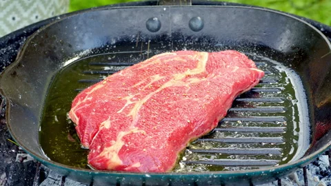 A red raw beef steak being fried in a cast iron pan with olive oil on a grill. Stock Footage 315904655