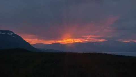 Red rays of the midnight sun through the clouds over the mountains Stock Photos