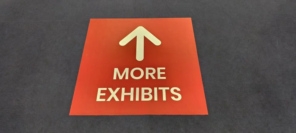 Red rectangular floor sign with text reading “MORE EXHIBITS.” Foto stock