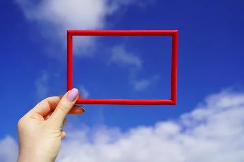 Red rectangular horizontal frame in female hand against blue sky. Bright spac Stock Photos