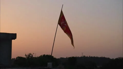 Red religious flag waving on a rooftop against a soft sunset sky Vidéo 333451371