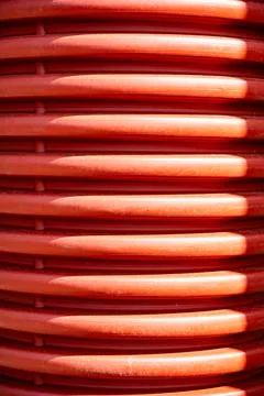 Red ribbed plastic pipe surface with sunlight creating abstract lines and Stock Photos