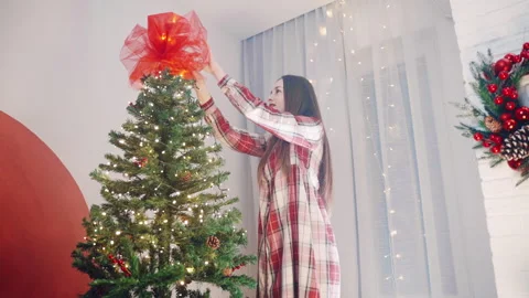 Red ribbon on the top of spruce tree, smiling woman decorating home interior for 库存影片 255376720