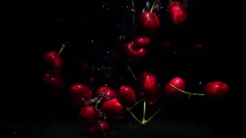 Red ripe cherries falling into water on black background. Stockbeeldmateriaal 200989113