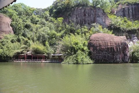 The red rock boulder of a mountain is surrounded by green vegetation, and t.. Stock Photos
