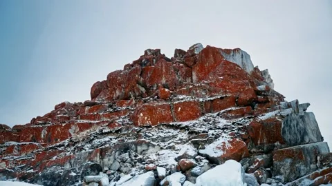 A red rock of rocks, covered in red lichen and covered in snow. Lake Baikal Stock-Footage 228883320