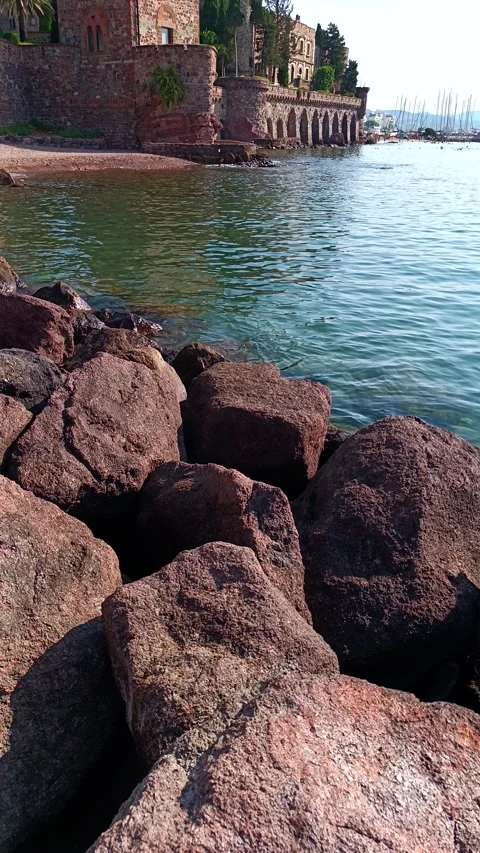Red rocks in foreground of a historic stone castle on the French coast Stock Footage 346124576