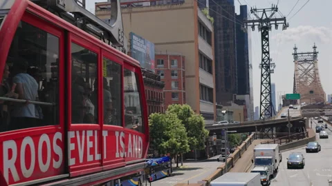 Red Roosevelt Island Tramway cabin passes Queensboro Bridge traffic. Stock Footage 346985714