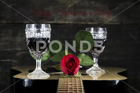 Red Rose and Wine Glasses Resting On Acoustic Guitar With Sign Happy Valent.. Stock Photos