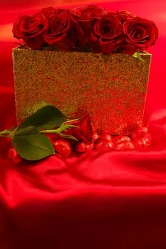Red roses in a gift box on red background with chocolate hearts scattered around Stock Photos