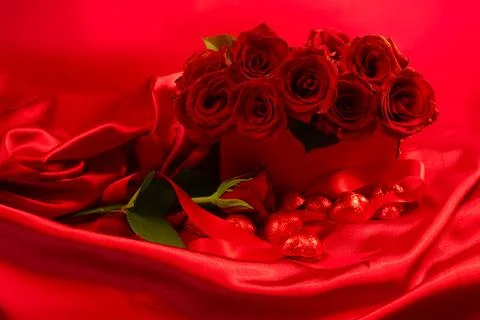 Red roses in a gift box on red background with chocolate hearts scattered around Stock Photos