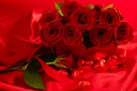 Red roses in a gift box on red background with chocolate hearts scattered around Stock Photos