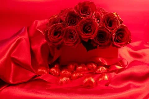 Red roses in a gift box on red background with chocolate hearts scattered around Stock Photos