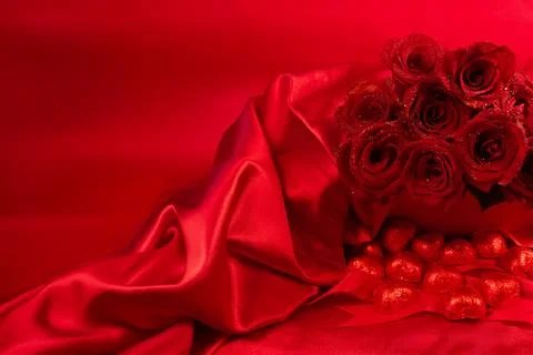 Red roses in a gift box on red background with chocolate hearts scattered around Stock Photos