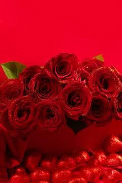 Red roses in a gift box on red background with chocolate hearts scattered around Stock Photos
