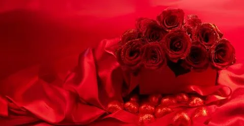 Red roses in a gift box on red background with chocolate hearts scattered around Stock Photos