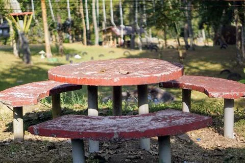 Red round concrete table and curved bench set in an open green park area. Stock Photos