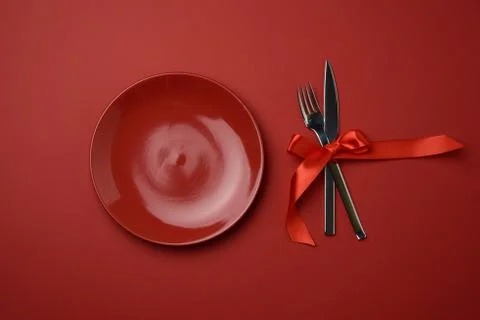 Red round empty ceramic plate and metal fork and knife tied with a red silk r Stock Photos