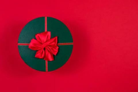 Red round gift box with a red bow on a green lid on a red background. View from Stock Photos