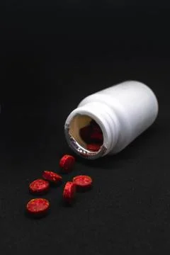 Red round supplement pills falling out a bottle Stock Photos