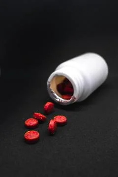 Red round supplement pills falling out a bottle Stock Photos