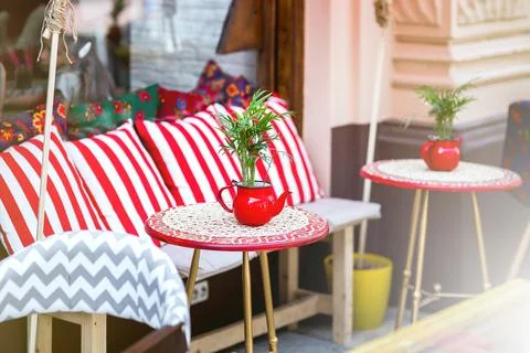A red round table with a tablecloth and a flowerpot in the form of a teapot. Stock Photos