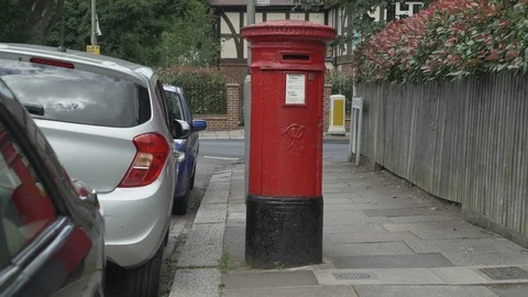 A Red Royal Mail Post box with a Royal Mail car passing by on a Stock Footage 111220426