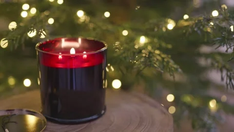 Red scented candle burning by Christmas tree with warm festive lights, 4K Stock Footage 324595053