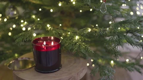 Red scented candle burning by Christmas tree with warm festive lights, 4K Stock Footage 324595059